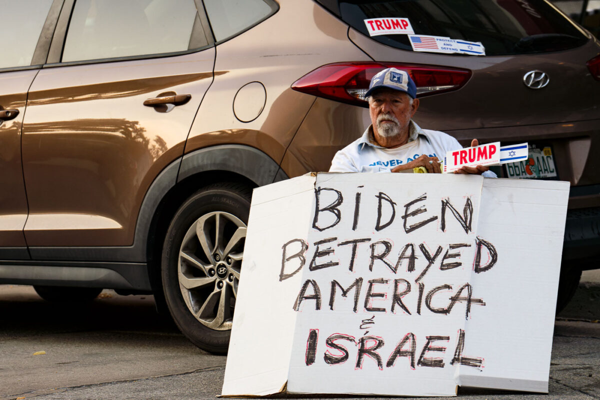 A man holding a sign and Trump and Israel bumper stickers near the 2024 Republican National Convention in Milwaukee.
