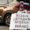 A man holding a sign and Trump and Israel bumper stickers near the 2024 Republican National Convention in Milwaukee.