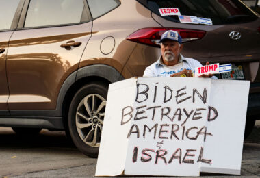 A man holding a sign and Trump and Israel bumper stickers near the 2024 Republican National Convention in Milwaukee.