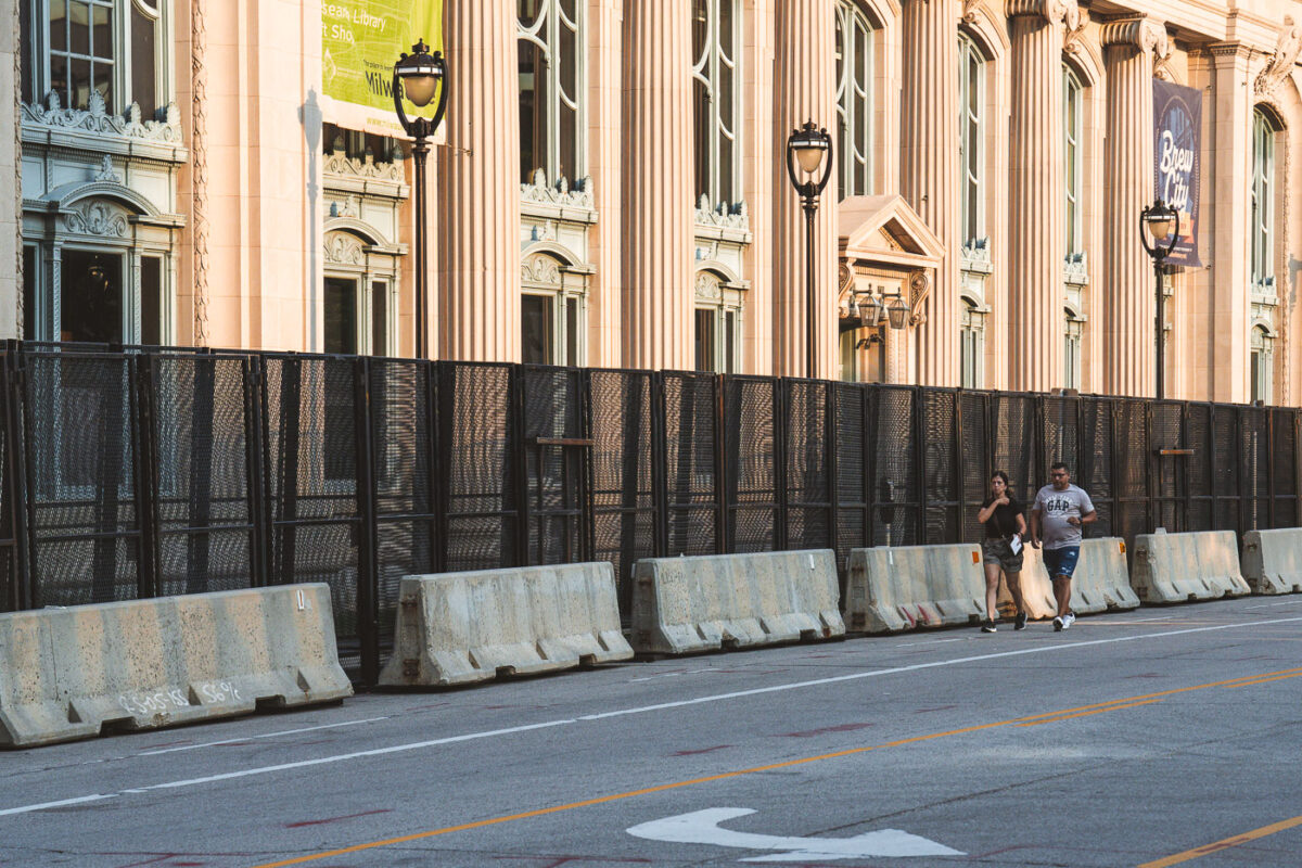 A couple walk outside security fencing surrounding theMilwaukee County Historical Society. The city is heavily secured during the 2024 Republican National Convention.