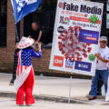 Man holds up a sign that reads "Fake media is the virus" and women hold hats that say "Stand with trump" "Never surrender". Never surrender began being used by supporters after Trump surrendered to Georgia authorities.