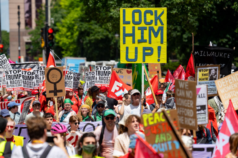 “Lock Him Up” Protest Sign at RNC Demonstration 3 A large yellow sign reading “Lock Him Up!” rises above a dense crowd of demonstrators near the 2024 RNC venue in Milwaukee. The protest blended national and local activist groups, with participants calling out issues ranging from reproductive rights to racial justice, while chanting and marching through the downtown area under a heavy police and media presence.⸻