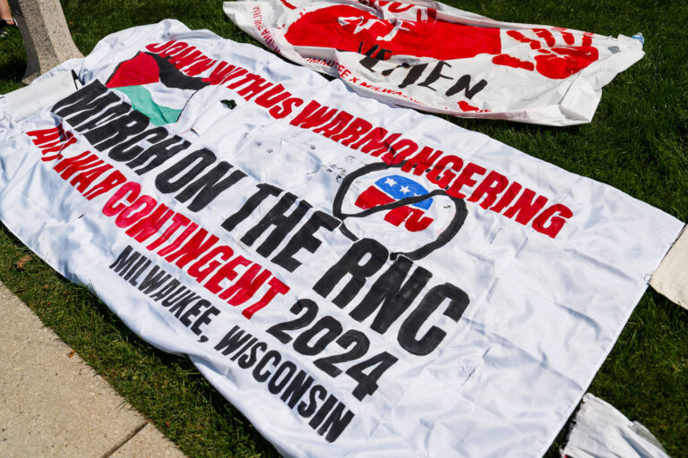 Antiwar Protest Banners Prepared for the 2024 RNC Demonstrations 4 Hand-painted banners lay across the grass in Milwaukee ahead of protests timed with the 2024 Republican National Convention. The slogans—such as “March on the RNC” and “Join with us against warmongering”—were created by antiwar coalitions and grassroots organizers rallying against U.S. foreign policy and political militarism.The banners’ bold red and black lettering, accompanied by imagery referencing Palestine and anarchist symbols, reflect the convergence of antiwar and pro-Palestine movements that framed much of the summer’s political dissent. Organizers from across the Midwest gathered for coordinated demonstrations in the city, part of a long tradition of convention-era activism stretching back to the 1968 DNC protests in Chicago.
