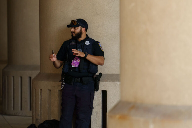Federal Officer on Duty Near Fiserv Forum During the 2024 RNC 2 A federal law enforcement officer stands at a post near the Fiserv Forum in Milwaukee, holding a communication device while overseeing a checkpoint area. Officers from multiple agencies—including the Secret Service, Capitol Police, and DHS task forces—were assigned to interior and exterior perimeters. Security staff operated under coordinated radio networks provided by federal command and the city’s Emergency Operations Center.