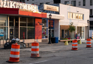Graffiti above Ragstock. An older couple walk down the under construction Lake Street.
