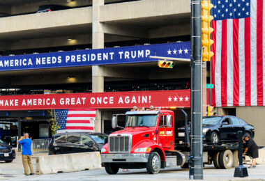 A car being towed near a parking ramp at the 2024 Republican National Convention. The ramp is wrapped with Make America Great Again branding.