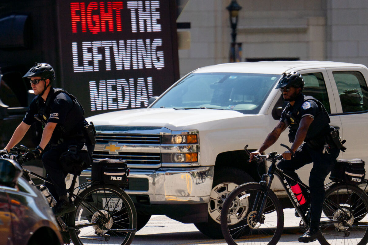 United States Capitol Police on bicycles at the 2024 Republican National Convention in Milwaukee. Biking by a "Fight the Leftwing Media" digital billboard.