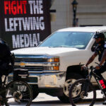 United States Capitol Police on bicycles at the 2024 Republican National Convention in Milwaukee. Biking by a "Fight the Leftwing Media" digital billboard.