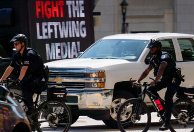 United States Capitol Police on bicycles at the 2024 Republican National Convention in Milwaukee. Biking by a "Fight the Leftwing Media" digital billboard.