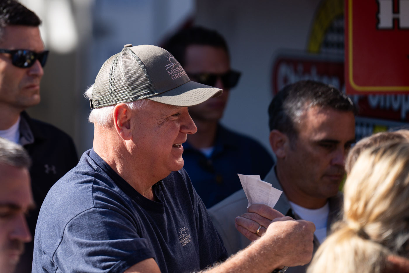 Governor Tim Walz at the Minnesota State Fair on Sept 1, 2024, wearing a "Minnesota Grown" cap and holding tickets.