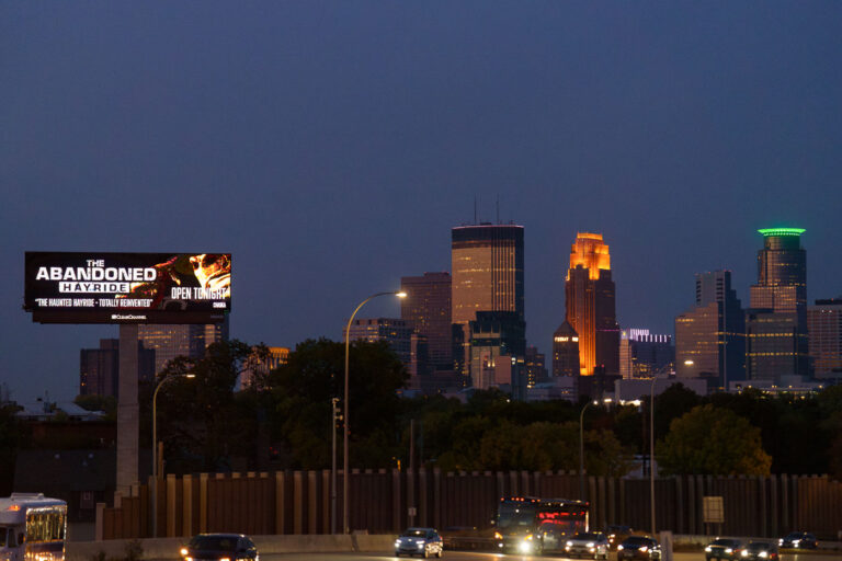 Abandoned Hayride Billboard on I-35W, Minneapolis Skyline 1 A digital billboard advertising "The Abandoned Hayride" is illuminated at dusk along Interstate 35W, with the Minneapolis skyline visible in the background. The billboard promotes the attraction as "The Haunted Hayride - Totally Reimagined" and indicates it is "Open Tonight." The Abandoned Hayride is a seasonal event typically held in Chaska, Minnesota, offering a Halloween-themed experience. Billboards like this serve as a common form of advertising for local entertainment and events, placed strategically along major thoroughfares to reach a broad audience.