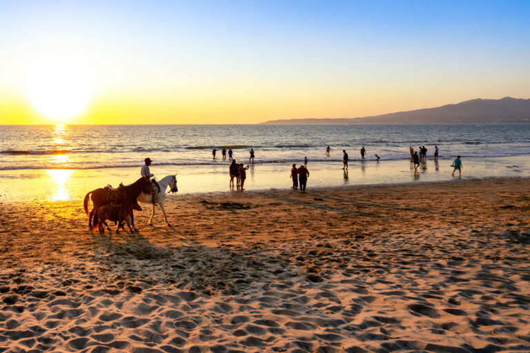 Evening at Puerto Vallarta Beach 2 Along the shoreline of Puerto Vallarta, Jalisco, people gather where the city meets the Pacific Ocean. Families cool off in the surf as the day winds down, while a local horse handler offers rides along the sand — a long-standing tradition of the bayfront. The beach, backed by the green ridges of the Sierra Madre, remains one of the central gathering spaces for Vallarta residents and visitors alike, blending tourism, community, and everyday coastal life.