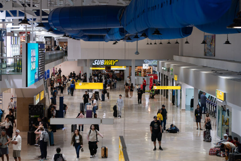 Travelers in Terminal at Puerto Vallarta International Airport 1 Passengers move through the arrivals and departures concourse at Puerto Vallarta International Airport (Licenciado Gustavo Díaz Ordaz International Airport), a major gateway for visitors to the Pacific coast. The yellow signage directs travelers toward check-in counters and baggage claim as people queue at kiosks and cafés like Subway and AeroMarket. The space, marked by distinctive blue air ducts and polished stone floors, reflects the airport’s recent modernization—balancing local efficiency with the flow of international tourism feeding the resorts along Bahía de Banderas.