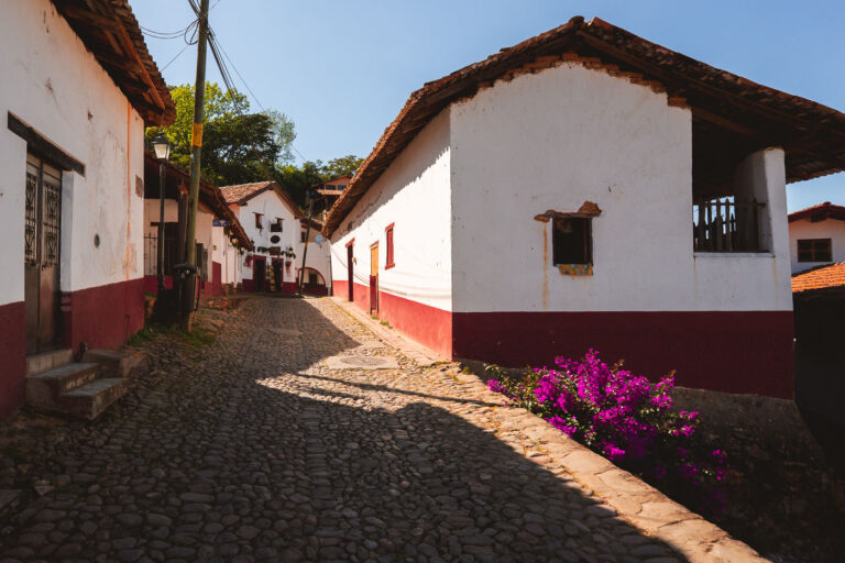 Cobblestone Street in San Sebastián del Oeste 4 A quiet cobblestone street winds through the historic center of San Sebastián del Oeste, a mountain town tucked into the Sierra Madre Occidental of Jalisco. The preserved adobe houses, painted in the traditional red-and-white palette with tiled roofs, evoke its 17th-century mining heritage. This view captures the town’s timeless character—narrow lanes, rustic façades, and bursts of bougainvillea that frame the colonial-era charm of one of Mexico’s most atmospheric Pueblos Mágicos.