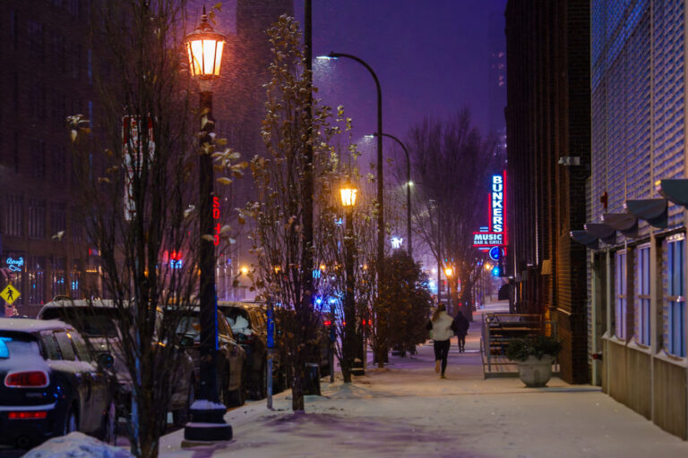 Night Snowfall, Bunker's, Washington Ave, Minneapolis, 2025 1 A snowfall blankets Washington Avenue in Minneapolis's North Loop district on January 9, 2025. Streetlights and neon signs from establishments such as Bunker’s Music Bar & Grill and Club Solo illuminate the street, which remains active despite the winter weather. The North Loop, historically an industrial area characterized by warehouses and rail spurs, has transformed into a significant center for music venues, restaurants, and bars. This district now serves as a lively urban environment where historic architecture coexists with contemporary businesses, maintaining its energy even during cold months.