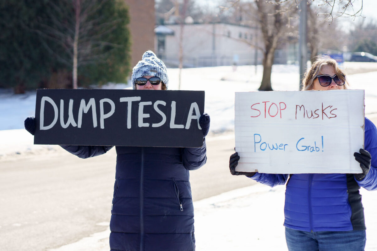 Protesters hold signs that read "Dump Tesla" "Stop Musk's Power Grab!" at a "Tesla Takeover" protest in front of a Tesla facility in Minneapolis on February 22, 2025.