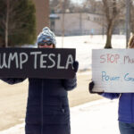 Protesters hold signs that read "Dump Tesla" "Stop Musk's Power Grab!" at a "Tesla Takedown" protest in front of a Tesla facility in Minneapolis on February 22, 2025.