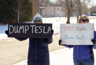 Protesters hold signs that read "Dump Tesla" "Stop Musk's Power Grab!" at a "Tesla Takedown" protest in front of a Tesla facility in Minneapolis on February 22, 2025.