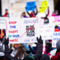 Protester at the Minnesota State Capitol on February 5, 2025 holding up a sign that reads "Stop the theft of our info!" "Absolutely no one voted for elon musk! None of us!".