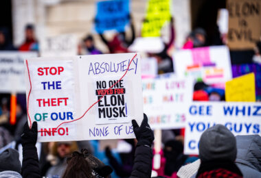 Protester at the Minnesota State Capitol on February 5, 2025 holding up a sign that reads "Stop the theft of our info!" "Absolutely no one voted for elon musk! None of us!".