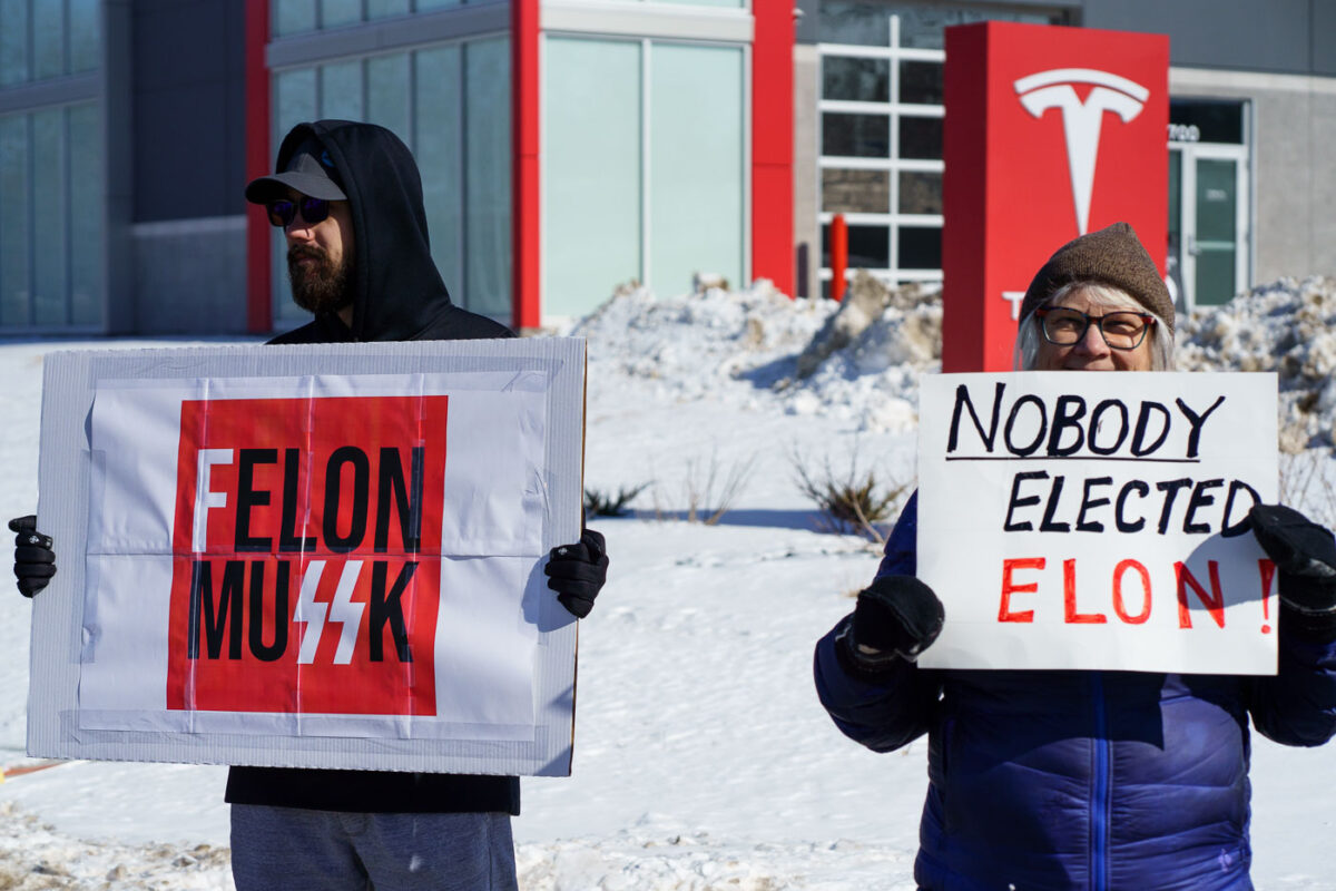 Protesters hold up signs that read "Felon MuSSK" "Nobody Elected Elon!" at a "Tesla Takeover" protest in front of a Tesla facility in Minneapolis on February 22, 2025.