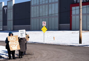 Protesters hold up signs reading "No Kings (Except Drag Kings) "Reminder: Nazi's Are Bad" at a "Tesla Takedown" protest in front of a Tesla facility in Minneapolis on February 22, 2025.