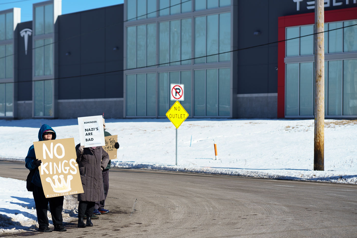 Protesters hold up signs reading "No Kings (Except Drag Kings) "Reminder: Nazi's Are Bad" at a "Tesla Takeover" protest in front of a Tesla facility in Minneapolis on February 22, 2025.