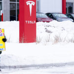 A man stands with a sign reading "Say No To Doge! Who Elected Musk President?" outside a Tesla facility in Minneapolis.