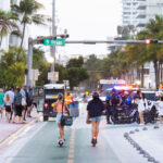 Spring breakers on scooters head past a group of police officers in South Beach during 2025 Spring Break in Miami Beach.