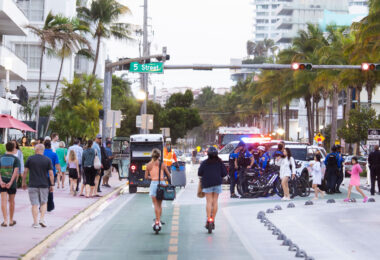Spring breakers on scooters head past a group of police officers in South Beach during 2025 Spring Break in Miami Beach.