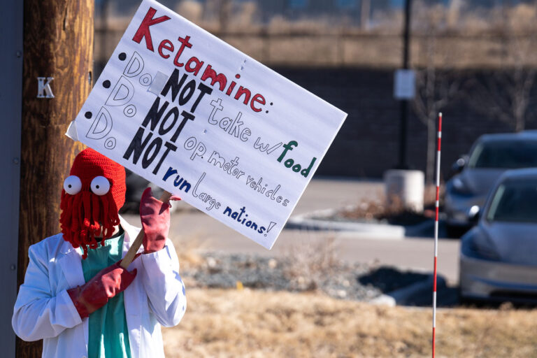 Elon Musk Ketamine Protest Sign 4 Protester in Minneapolis (Golden Valley) holds up a protest sign at a Tesla facility.