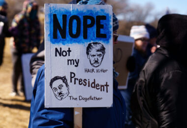 Protester holding up a sign that reads 

"Nope Not my President"

"Hair Hitler"
"The Dogefather"

Protesters have gathered each Saturday for weeks now at this Tesla Facility just outside of Minneapolis (Golden Valley).