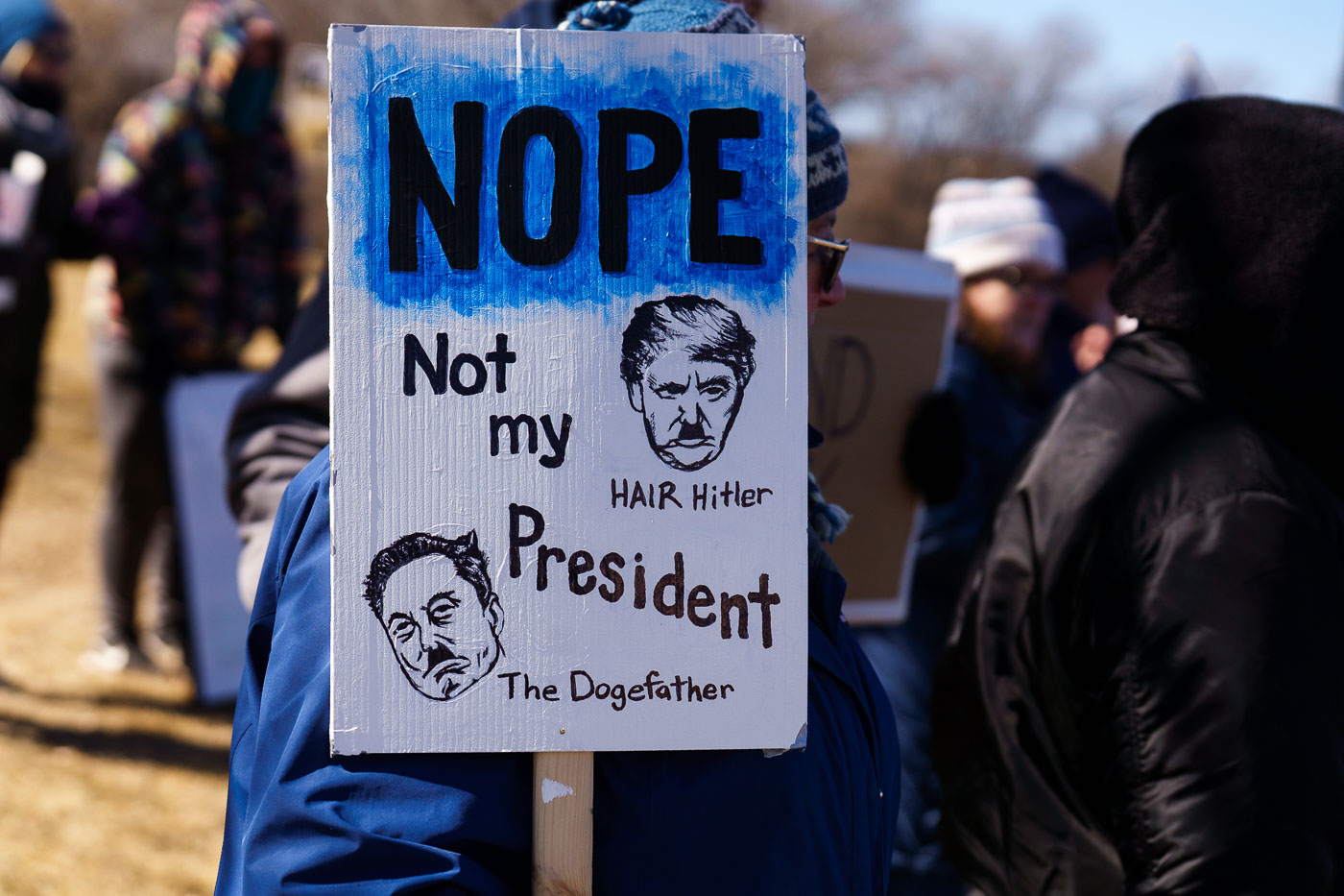 Protester holding up a sign that reads "Nope Not my President""Hair Hitler""The Dogefather"Protesters have gathered each Saturday for weeks now at this Tesla Facility just outside of Minneapolis (Golden Valley).