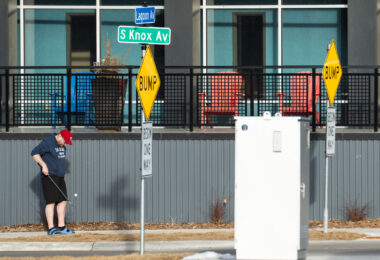 A man with a golf club and ball in Uptown Minneapolis on the first 60 degree day of the year.