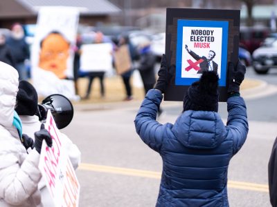 "Nobody Elected Musk" Sign Raised Above Tesla Protest Crowd
