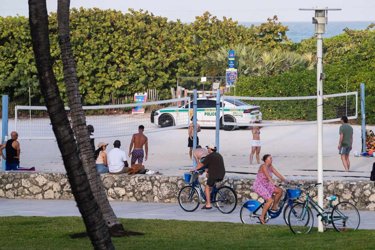Squad car drives down past a volleyball game in south beach