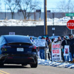 A Tesla car drives by a group of protesters in Golden Valley (Minneapolis). The protesters have been gathering for weeks as part of "Tesla Takedown" protests.