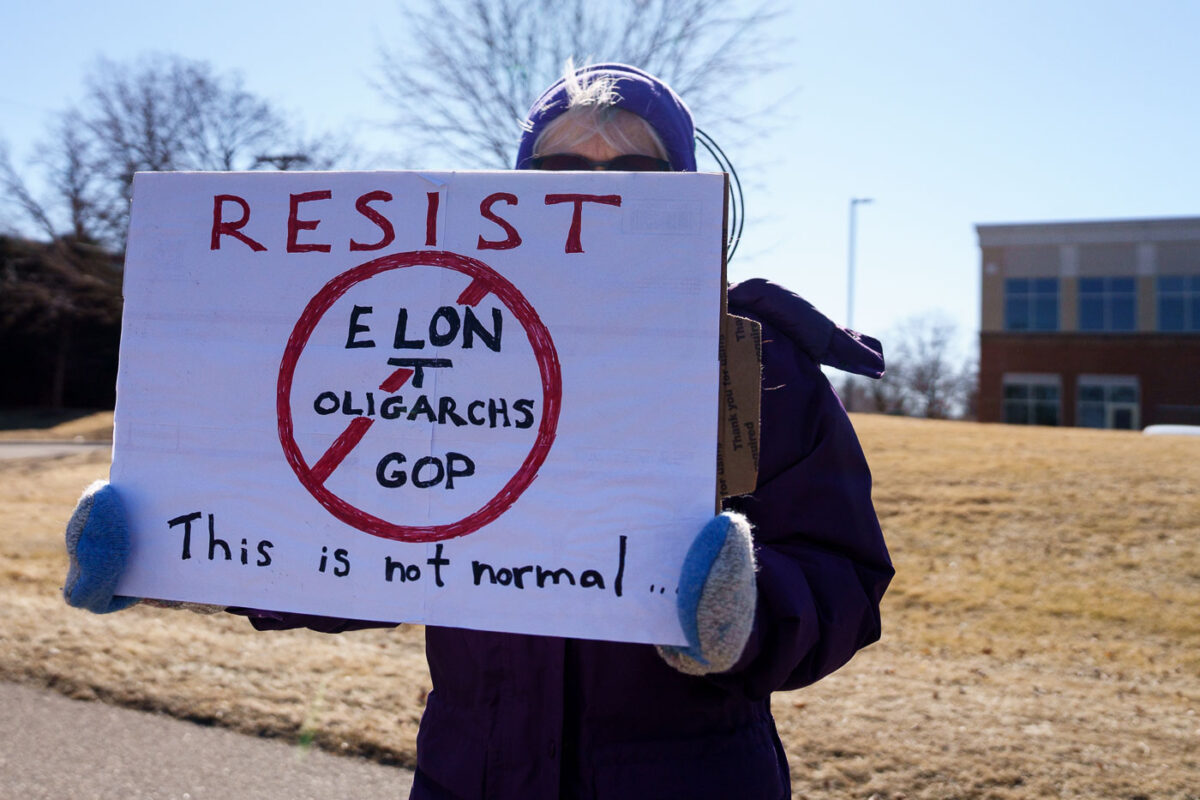 Protester holding up a sign that reads "Resist Elon Tesla Oligarchs GOP This is not normal" outside a Tesla facility in just outside of Minneapolis (Golden Valley) on March 1st, 2025. 

This is the third weekend in a row they've gathered to protest the actions of Elon Musk and the current administration