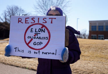 Protester holding up a sign that reads "Resist Elon Tesla Oligarchs GOP This is not normal" outside a Tesla facility in just outside of Minneapolis (Golden Valley) on March 1st, 2025. 

This is the third weekend in a row they've gathered to protest the actions of Elon Musk and the current administration