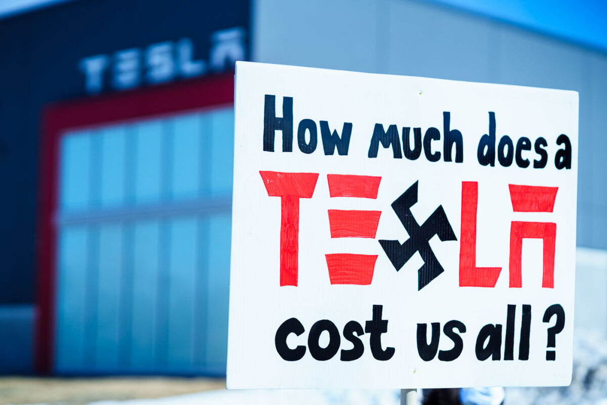 Protester holds a sign that reads "How much does Tesla cost us all?". Seen at a Tesla facility just outside of Minneapolis (Golden Valley) on March 8, 2025.

This is the 4th week in a row protesters have gathered here as part of the nationwide Tesla Takedown organizing.