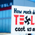 Protester holds a sign that reads "How much does Tesla cost us all?". Seen at a Tesla facility just outside of Minneapolis (Golden Valley) on March 8, 2025.

This is the 4th week in a row protesters have gathered here as part of the nationwide Tesla Takedown organizing.