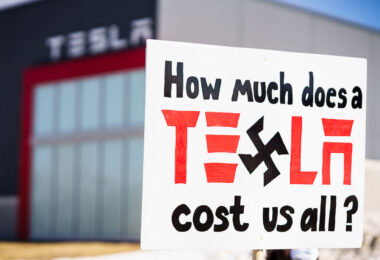 Protester holds a sign that reads "How much does Tesla cost us all?". Seen at a Tesla facility just outside of Minneapolis (Golden Valley) on March 8, 2025.

This is the 4th week in a row protesters have gathered here as part of the nationwide Tesla Takedown organizing.