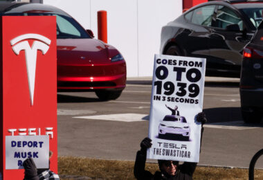 Protesters hold up signs reading "Deport Musk" and "Tesla The Swasticar" at a protest outside a Tesla facility in Minneapolis(Golden Valley) on March 1, 2025. The protests are part of nationwide "Tesla Takedown" protests targeting Musk, Tesla and the Trump Administration.