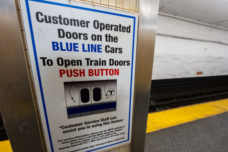 A platform sign explaining customer-operated doors on Blue Line trains of the Massachusetts Bay Transportation Authority. Unlike many rapid-transit systems where doors open automatically at every stop, portions of the MBTA Blue Line fleet require passengers to press a button to open the doors once the train is stopped. This practice dates back to older car designs and cold-weather operating considerations, helping retain heat in winter and reduce unnecessary door cycling. The sign reflects the MBTA’s continued reliance on legacy rolling stock and the need for clear, standardized instructions in stations with high passenger turnover.