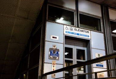 An elevator entrance at Bowdoin station, the downtown terminal of Boston’s Blue Line. Bowdoin Station opened in 1916 as part of the East Boston Tunnel, one of the earliest underwater rapid-transit tunnels in North America. The station is notable for its compact footprint, tight curves, and historically limited accessibility compared to newer MBTA stations.

This elevator provides step-free access between street level and the platform, reflecting later retrofits required by accessibility standards rather than original station design. The utilitarian signage, metal paneling, and enclosed structure are characteristic of mid-to-late 20th century upgrades layered onto early 20th century transit infrastructure, illustrating how legacy subway systems have been incrementally adapted to modern accessibility and safety requirements.