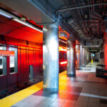 Haymarket Station, Orange Line Platform 3 Haymarket Station in downtown Boston, one of the oldest transit locations in the city, serving riders since the late 19th century in various forms. The current underground station opened in 1971 as part of the MBTA’s modernization of the Orange Line, replacing earlier elevated structures that once ran through the area. The station sits at the edge of the historic Haymarket district, long associated with public markets and transportation links between downtown and Boston’s North End. The cylindrical steel columns and low-ceilinged platforms reflect mid-20th-century transit design, while the signage and lighting document decades of incremental updates to keep the station functional within one of the system’s busiest transfer points.