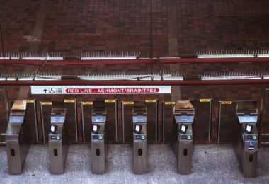 Fare gates line the paid entrance to the Massachusetts Bay Transportation Authority Red Line, directing riders toward Alewife-bound service. This northbound branch terminates at Alewife, the line’s northern endpoint, and serves as a primary commuter gateway for Cambridge and the Route 2 corridor. The stainless-steel fare control equipment reflects systemwide upgrades rolled out during the 2010s to improve ADA accessibility, reliability, and compatibility with modern fare media. Above the gates, the brick-vaulted ceiling and exposed utilities reflect the durable, utilitarian architecture common to many core Boston subway stations built and expanded in the mid-20th century, prioritizing longevity and fire resistance in high-traffic underground spaces.