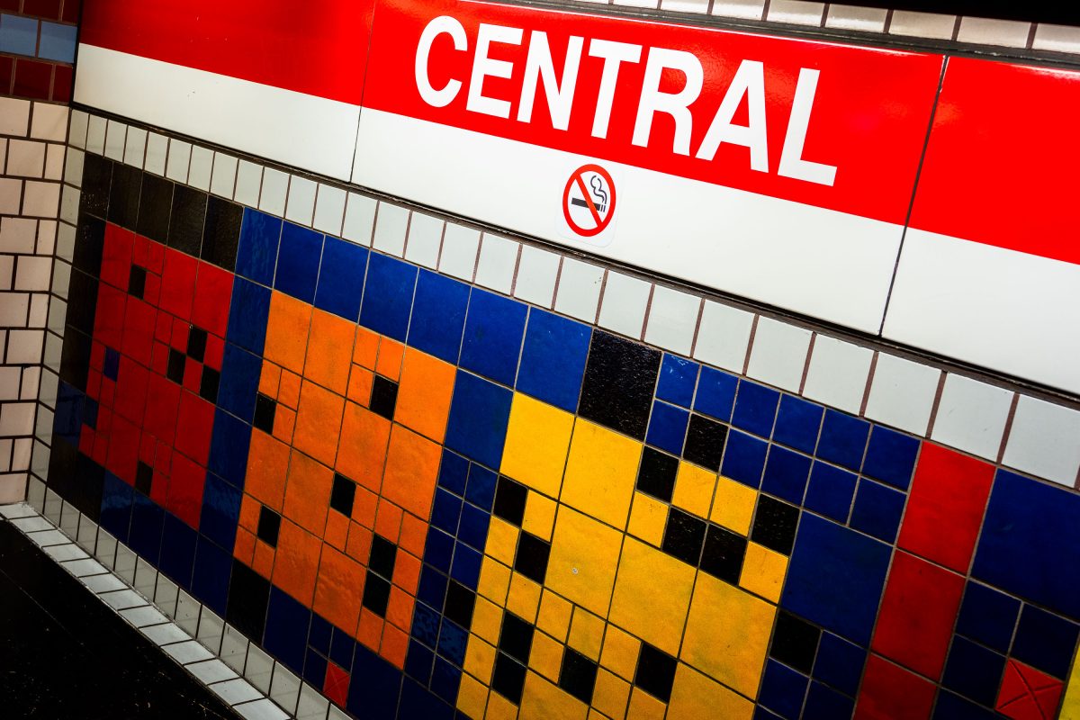 Central MBTA station sign above colorful pixelated tile mosaic in red, orange, yellow, and blue.