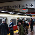 Red Line Inbound Platform, Downtown Boston 1 Passengers wait alongside an inbound MBTA Red Line train, headed toward Alewife, on a busy underground platform in downtown Boston. The Red Line is the system’s oldest rapid transit route, opening in 1912 and forming the backbone of east–west and north–south travel through the city. The high-floor cars shown here reflect decades of incremental fleet updates, while the tiled platforms, overhead wayfinding, and digital countdown signs illustrate how the MBTA has layered modern passenger information systems onto early-20th-century station infrastructure. The crowding and luggage visible on the platform highlight the line’s dual role serving both daily commuters and airport-bound travelers via transfers to bus and rail connections.