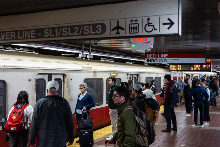 Red Line Inbound Platform, Downtown Boston 3 Passengers wait alongside an inbound MBTA Red Line train, headed toward Alewife, on a busy underground platform in downtown Boston. The Red Line is the system’s oldest rapid transit route, opening in 1912 and forming the backbone of east–west and north–south travel through the city. The high-floor cars shown here reflect decades of incremental fleet updates, while the tiled platforms, overhead wayfinding, and digital countdown signs illustrate how the MBTA has layered modern passenger information systems onto early-20th-century station infrastructure. The crowding and luggage visible on the platform highlight the line’s dual role serving both daily commuters and airport-bound travelers via transfers to bus and rail connections.